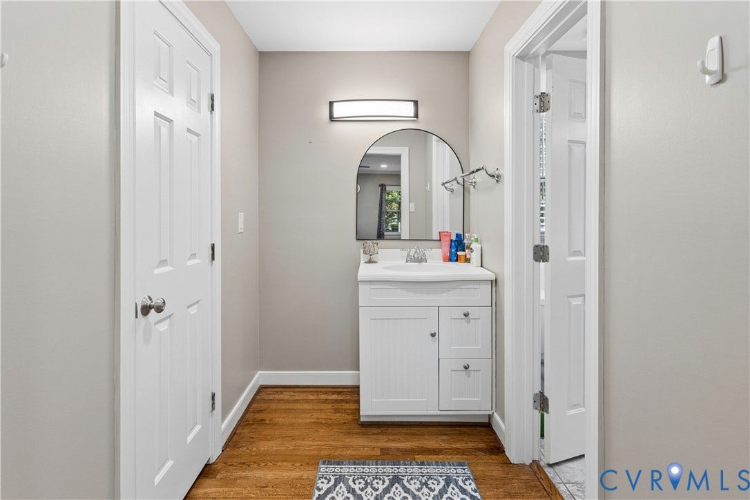 327 Huddersfield Drive, Chesterfield, VA 23236 White vanity cabinet featuring an integrated sink, polished chrome hardware, arch-top wall mirror, wall-mounted light fixture, and wood-finish flooring