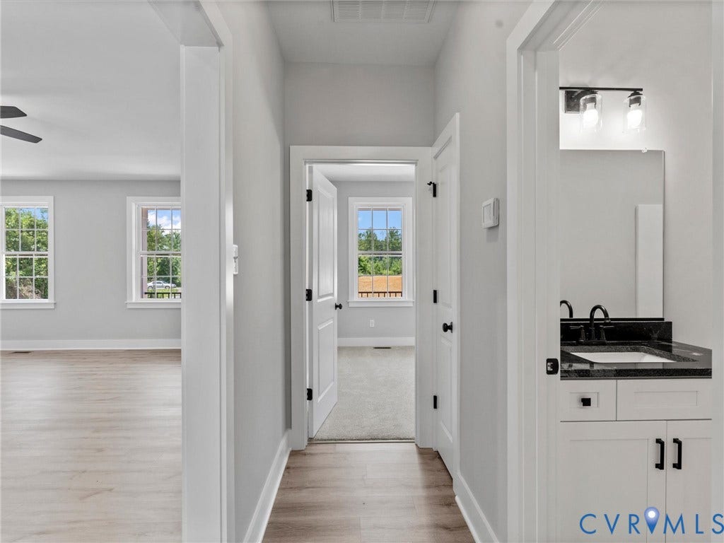 5951 Pot Rock Lane, Pot Rock Ln, Jetersville, VA 23083 Neutral interior hallway featuring wood-finish flooring, white shaker-style cabinetry with dark hardware, stone-top vanity, and dual-light wall sconce