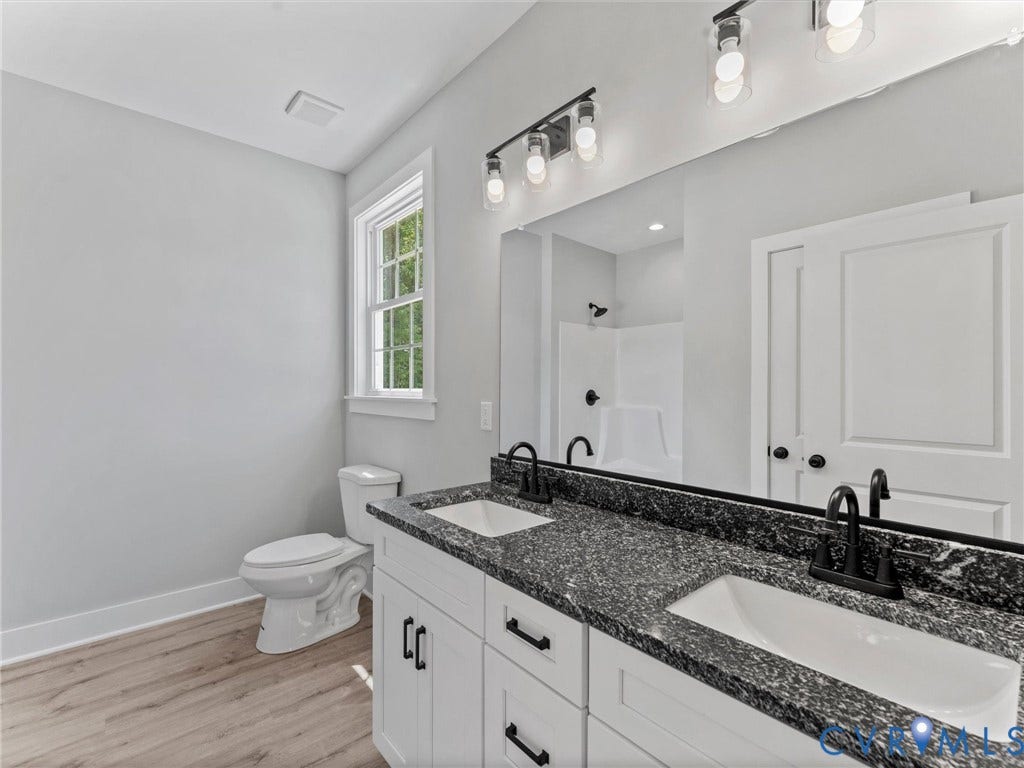 5951 Pot Rock Lane, Pot Rock Ln, Jetersville, VA 23083 Dual-sink vanity with dark stone-finish countertop, white cabinetry with matte black hardware, wood-finish flooring, and wall-mounted light fixtures