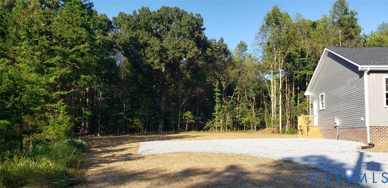5951 Pot Rock Lane, Pot Rock Ln, Jetersville, VA 23083 Exterior featuring grey horizontal siding, brick masonry base, crushed stone driveway, and a wood entry staircase, bordered by mature woodland