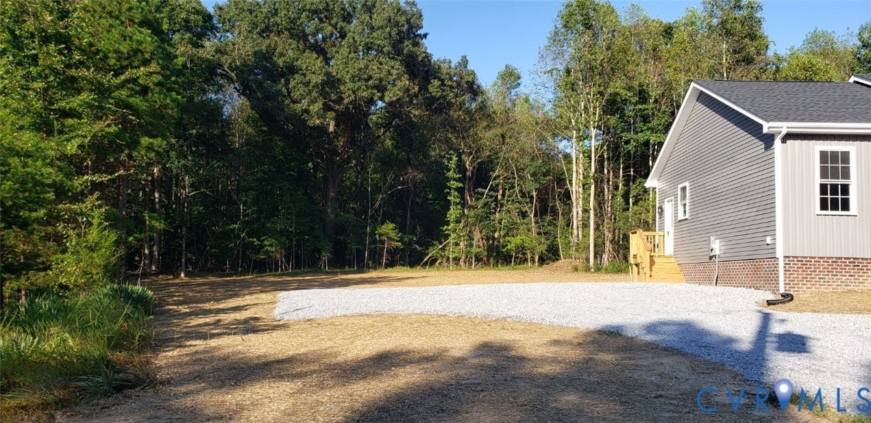 5951 Pot Rock Lane, Pot Rock Ln, Jetersville, VA 23083 Exterior featuring horizontal grey siding, brick foundation masonry, gravel driveway, wood-framed stairs, and dense perimeter forestry