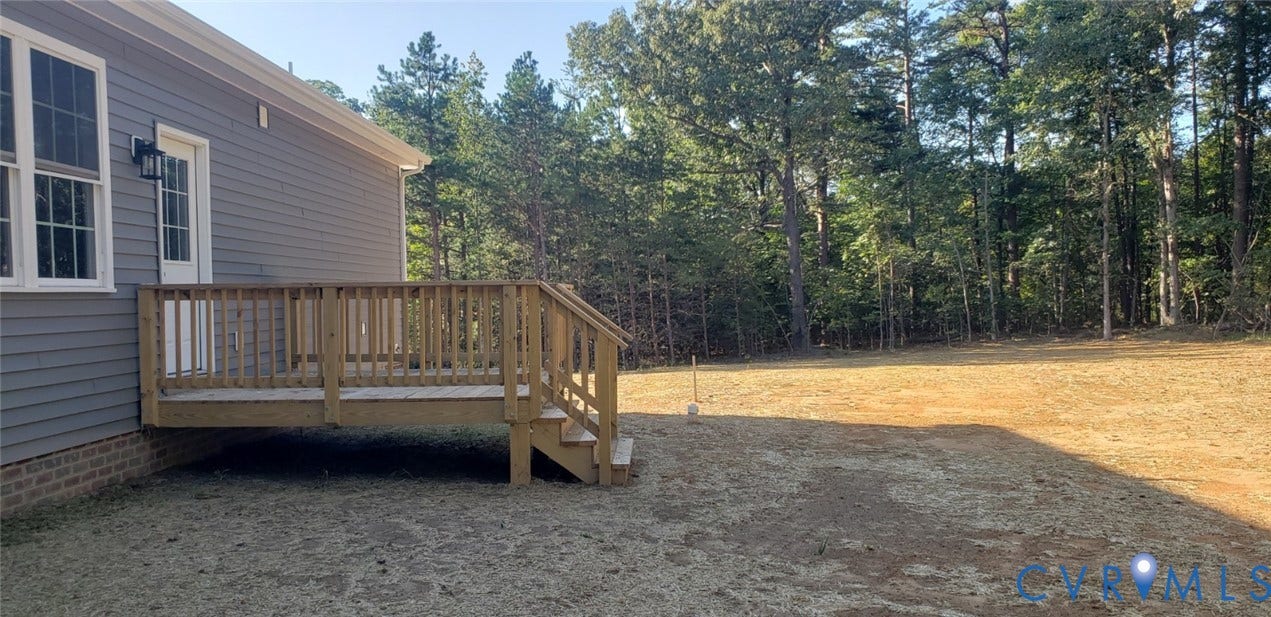 5951 Pot Rock Lane, Pot Rock Ln, Jetersville, VA 23083 Rear exterior featuring grey horizontal siding, a wood-framed deck, a brick foundation perimeter, and a lot bordered by mature trees