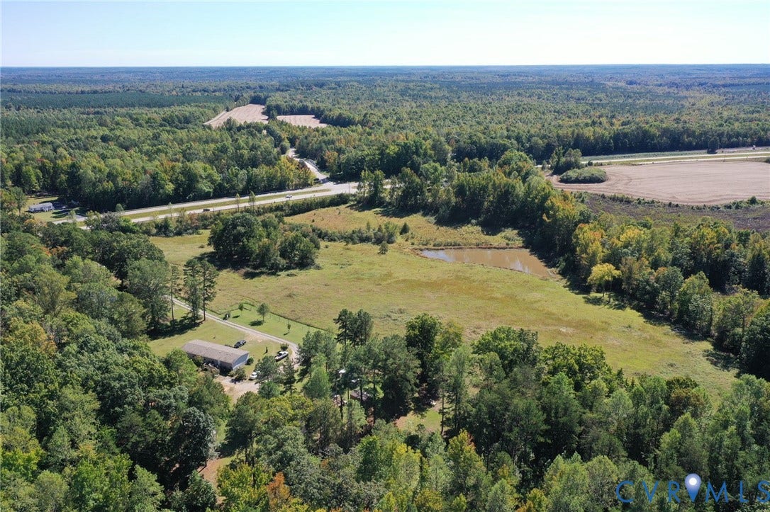 00 Patrick Henry HWY, Detached, Burkeville, VA 23922 Aerial perspective of a sprawling property featuring expansive open pastureland, a private pond, and established perimeter woodlands