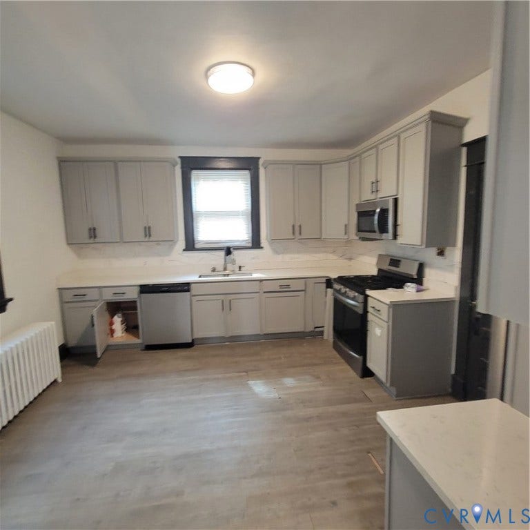 Kitchen featuring light-gray cabinetry, solid-surface countertops, stainless steel appliances, and wood-finish flooring