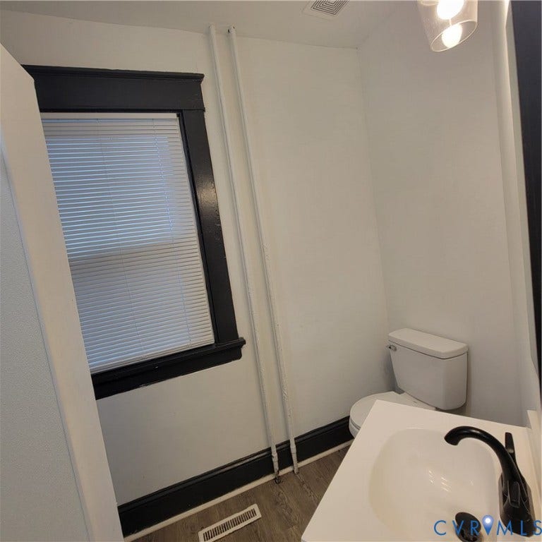 Restroom featuring a vanity with a white countertop, matte black faucet, wood-finish flooring, and high-contrast dark window trim