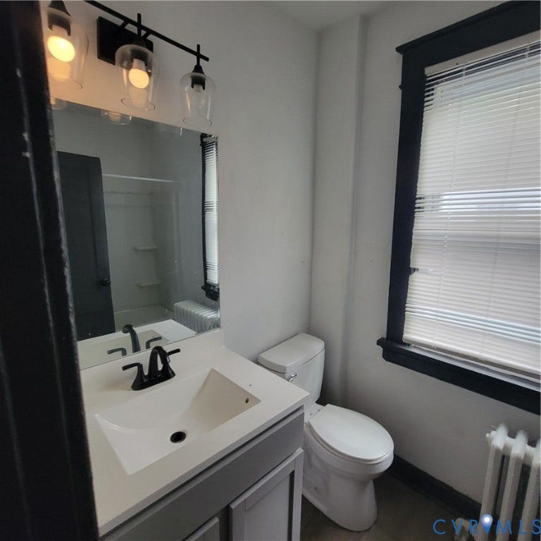 Bathroom featuring a vanity with a white countertop and integrated sink, matte black faucet, three-light fixture with glass shades, and dark-finished window casing