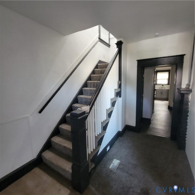 Staircase featuring a painted newel post, balusters, and a handrail, contrasted by doorway trim and carpeted steps