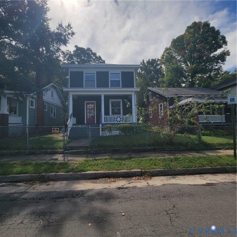 Two-story residence featuring a covered front porch, decorative balustrades, a paneled front door with glass inserts, and a chain-link fenced perimeter