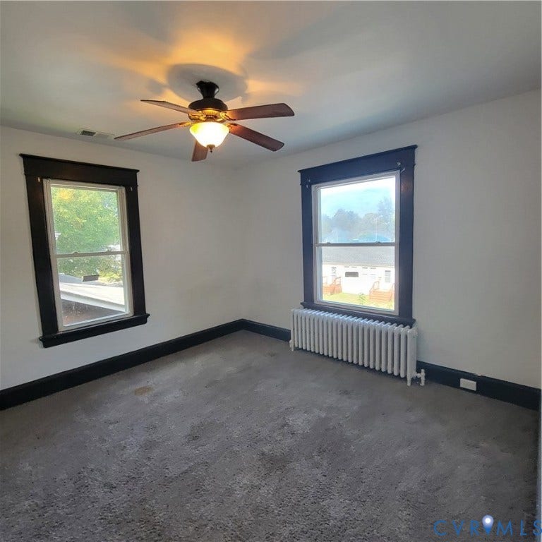 Room featuring dark-toned window casings, a ceiling fan with integrated lighting, and a metal radiator