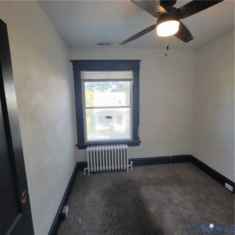 Interior space featuring high-contrast dark trim, wall-to-wall carpeting, a cast-iron radiator, and an integrated ceiling fan with a light fixture