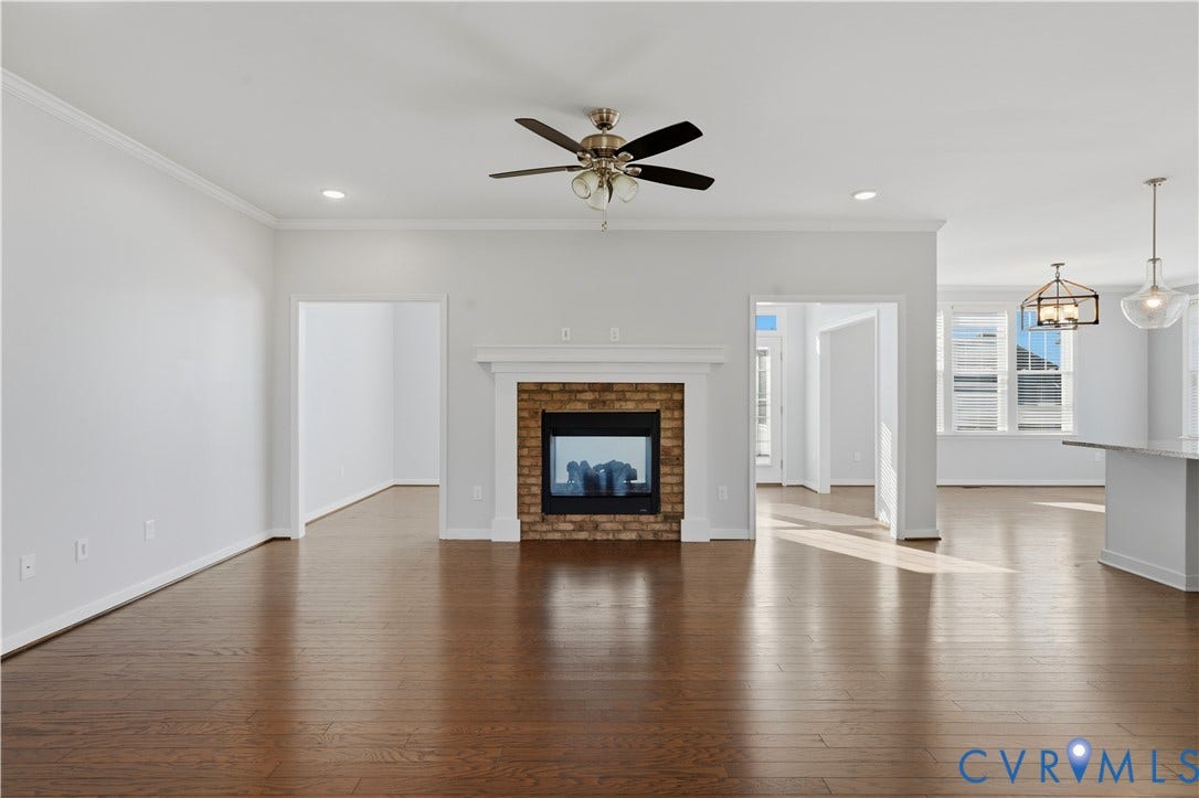 11936 Helmway Court, Chester, VA 23839 Open-concept interior featuring wood-finish flooring, brick-surround fireplace with a white mantel, ceiling fan with integrated lighting, and modern pendant fixtures
