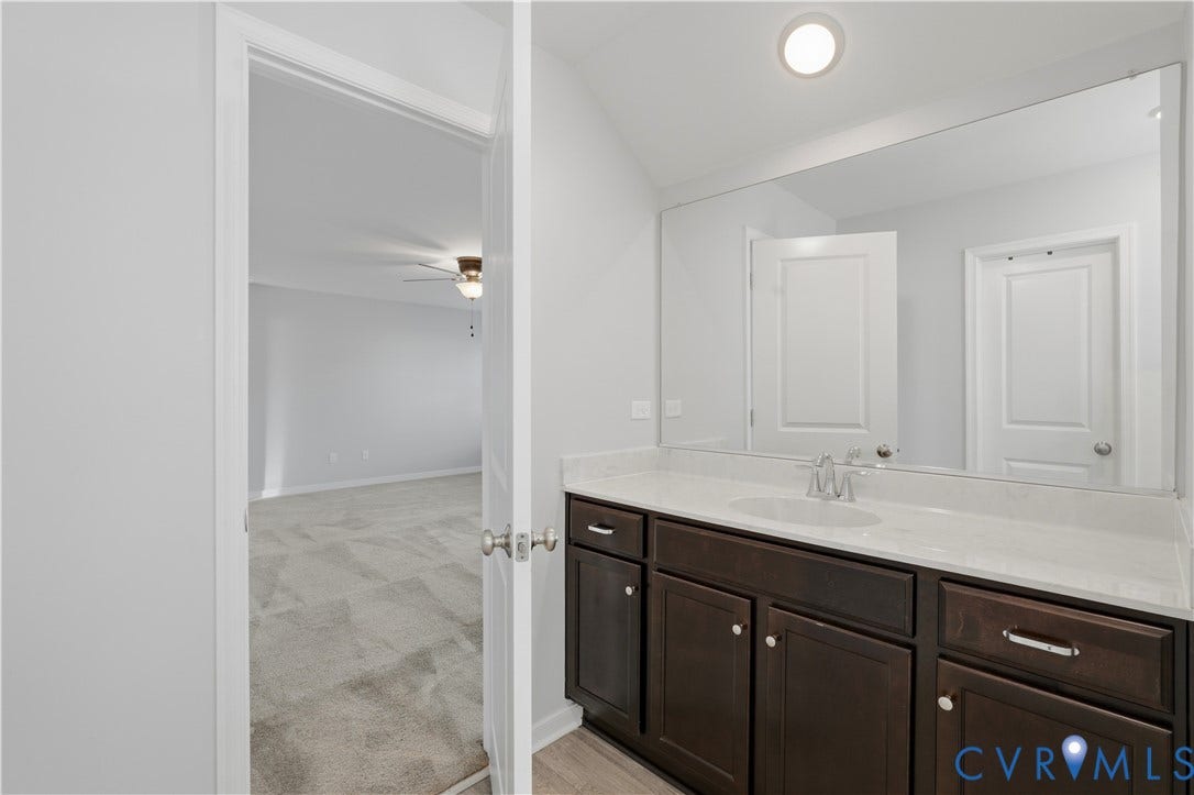 11936 Helmway Court, Chester, VA 23839 Upstairs Primary Bathroom vanity featuring dark-toned cabinetry, light-toned stone-finish countertop, integrated oval basin, and a large wall-mounted mirror