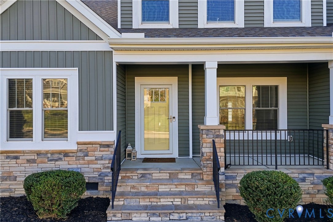 11936 Helmway Court, Chester, VA 23839 Exterior facade featuring sage green vertical and horizontal siding, stone veneer masonry, covered porch with square columns, and black metal railings