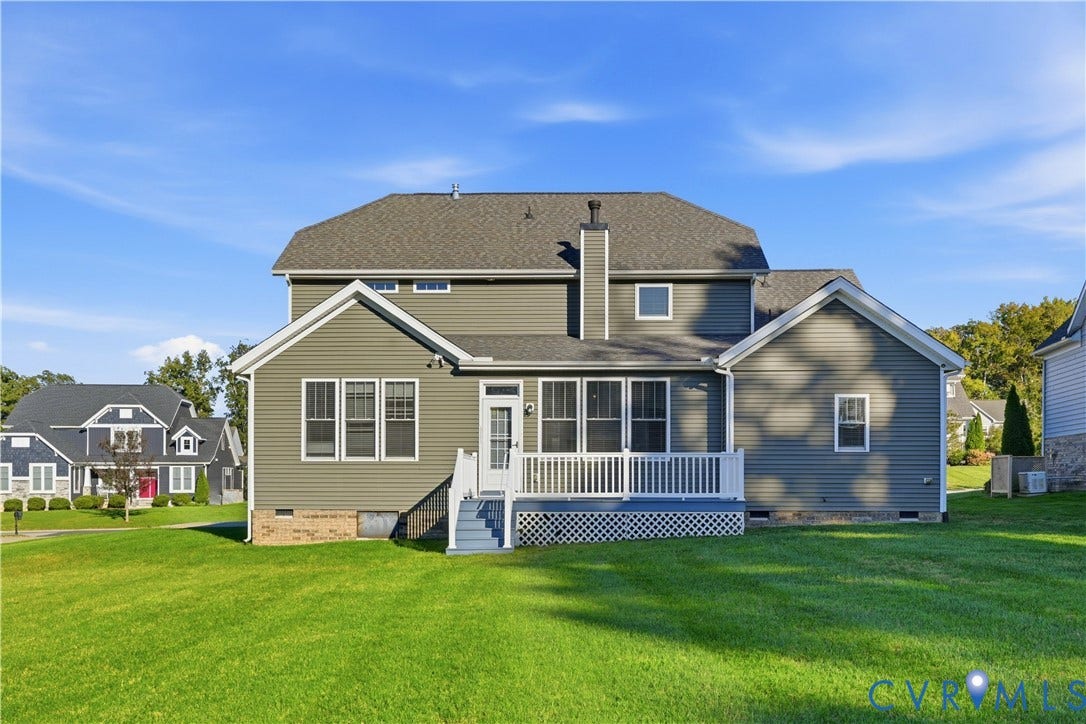 11936 Helmway Court, Chester, VA 23839 Rear exterior featuring gray horizontal siding, a central chimney, a raised deck with white railing, and a sprawling lawn