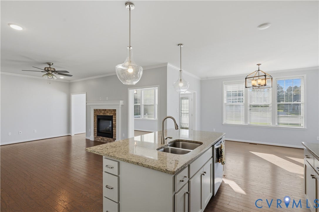 11936 Helmway Court, Chester, VA 23839 Kitchen island with stone-finish countertop, dual-basin stainless steel sink, wood-finish flooring, fireplace with brick surround, and pendant lighting
