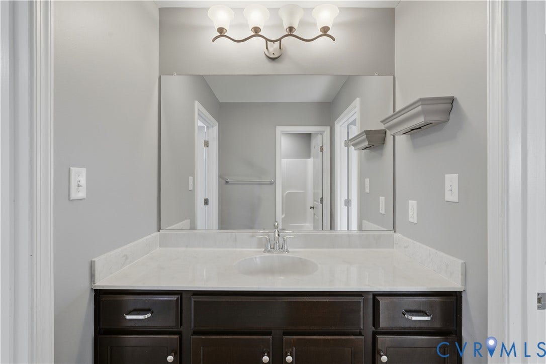 11936 Helmway Court, Chester, VA 23839 Jack and Jill upstairs bathroom. Dark-finish cabinetry with silver-tone hardware, stone-composite countertop with integrated sink, four-light vanity fixture, and large-format wall mirror