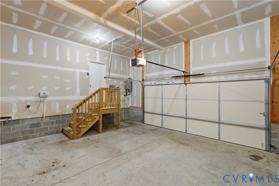 11936 Helmway Court, Chester, VA 23839 Two-car garage featuring a sectional overhead door, concrete flooring, exposed masonry block walls, and a built-in wooden staircase