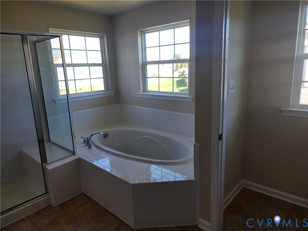 9031 Annex Lane, Mechanicsville, VA 23116 Oval soaking tub with a tiled surround, separate glass-enclosed shower, grid-pattern windows, and tile flooring