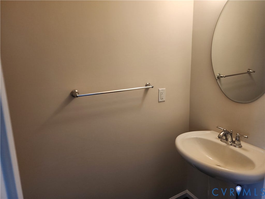 9031 Annex Lane, Mechanicsville, VA 23116 Pedestal sink with a two-handle chrome faucet, oval wall-mounted mirror, and brushed nickel towel bar