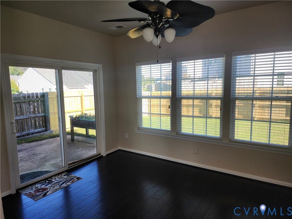 9031 Annex Lane, Mechanicsville, VA 23116 Dark-toned wood-finish flooring, sliding glass door, three windows with horizontal blinds, and a multi-blade ceiling fan with integrated lighting