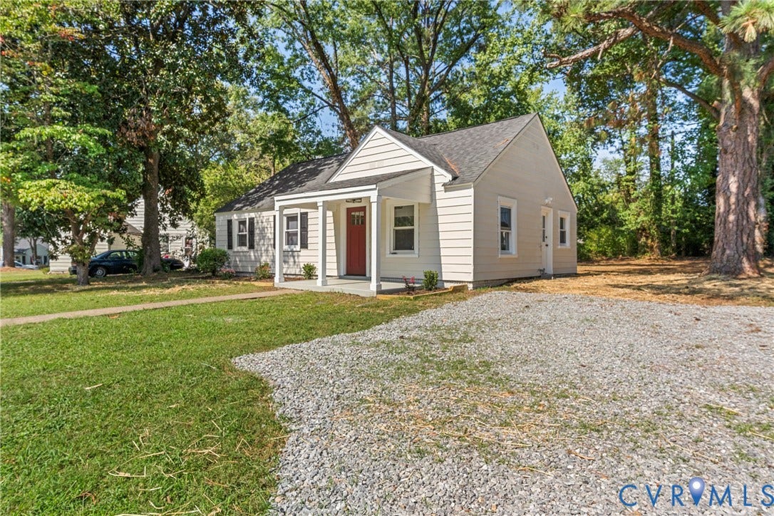 7406 Alycia Avenue, Henrico, VA 23228 Light-colored siding exterior with a red front door, covered porch, dark roof, and a gravel driveway