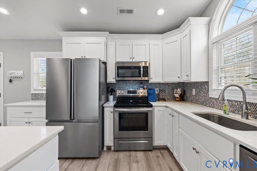 600 Highland Avenue, Hopewell, VA 23860 Kitchen featuring white shaker cabinetry, stainless steel appliances, mosaic tile backsplash, solid-surface countertops, and an arched window