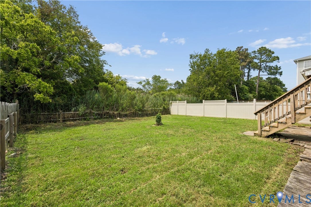 11 Bonita Drive, Hampton, VA 23664 Expansive backyard featuring a manicured lawn, perimeter vinyl fencing, mature trees, and wooden exterior staircase