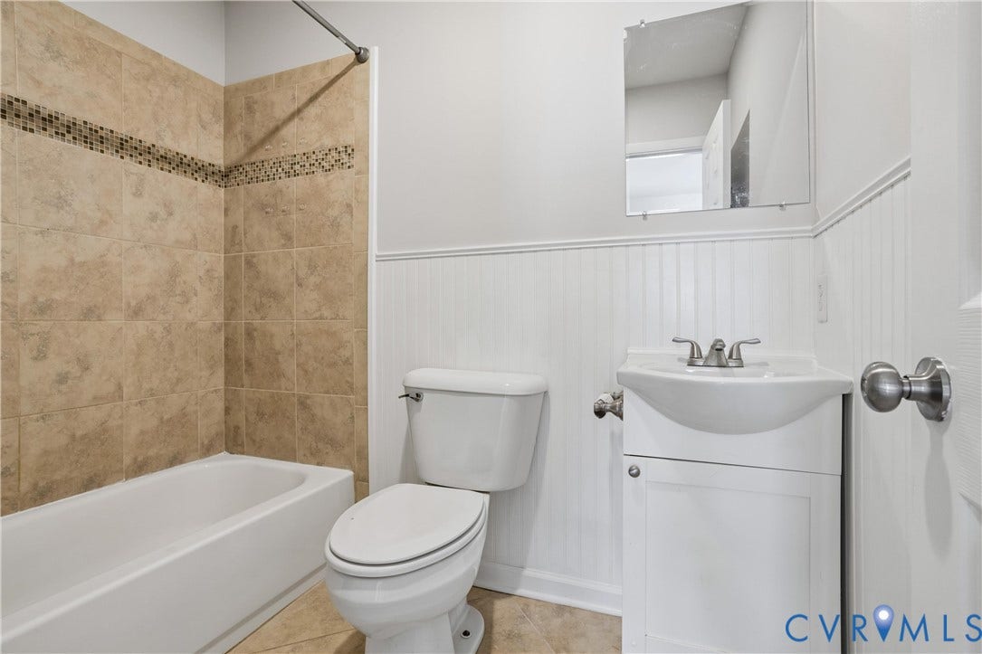 11 Bonita Drive, Hampton, VA 23664 Bathroom featuring a vanity with a pedestal-style sink, white beadboard wainscoting, and a tub enclosure with tan tile and a decorative mosaic accent band