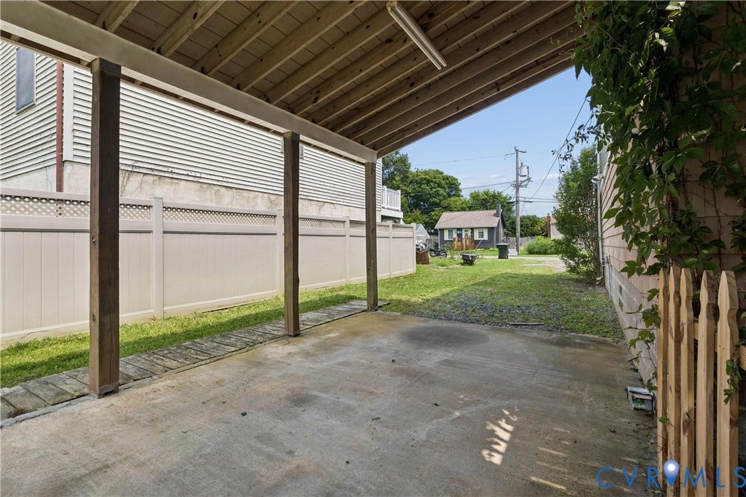 11 Bonita Drive, Hampton, VA 23664 Covered concrete carport featuring exposed wood rafters, vinyl perimeter fencing, and wood-slat partial screen