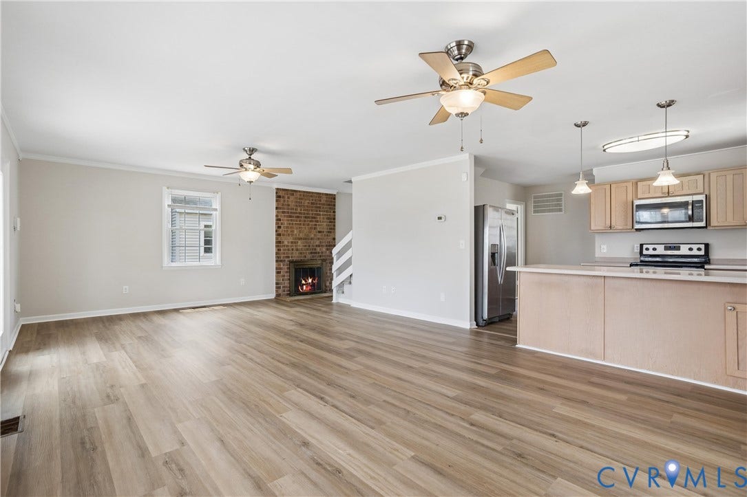11 Bonita Drive, Hampton, VA 23664 Open-concept living space featuring wood-finish flooring, a full-height brick fireplace, a peninsula kitchen with light-tone cabinetry, and dual ceiling fans
