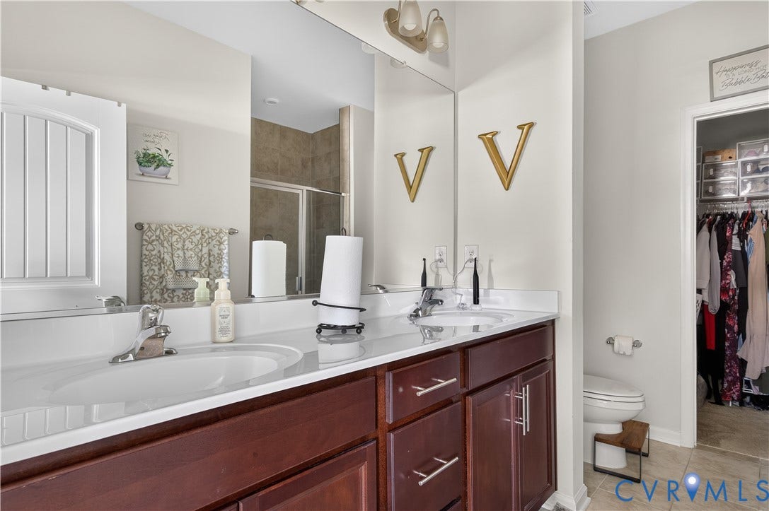 2230 Nightfall Drive, Chesterfield, VA 23236 Dual-sink vanity with dark wood-finish cabinetry, solid-surface countertop, full-width mirror, and chrome-finish hardware