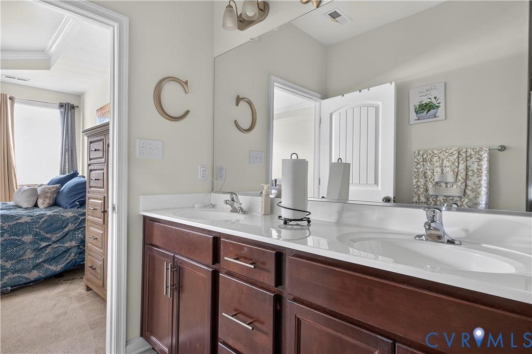 2230 Nightfall Drive, Chesterfield, VA 23236 Double vanity featuring dark wood-finish cabinetry, integrated white countertops with dual drop-in sinks, polished chrome faucets, and an expansive wall-mounted mirror