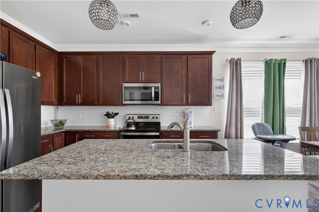 2230 Nightfall Drive, Chesterfield, VA 23236 Kitchen featuring dark wood cabinetry, a central island with an integrated stainless steel double-basin sink, stone countertops, a subway tile backsplash, and two spherical pendant lights