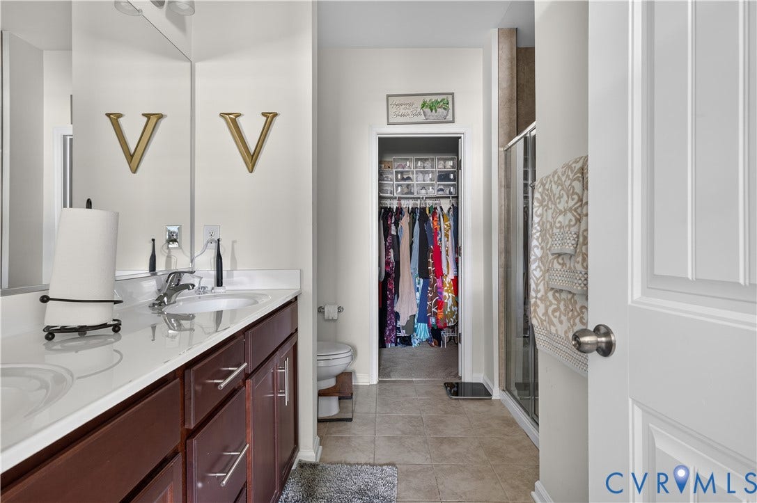 2230 Nightfall Drive, Chesterfield, VA 23236 Double vanity featuring a light-toned countertop with integrated dual sinks, dark wood-finish cabinetry, full-width mirror, glass-enclosed shower, and tile flooring