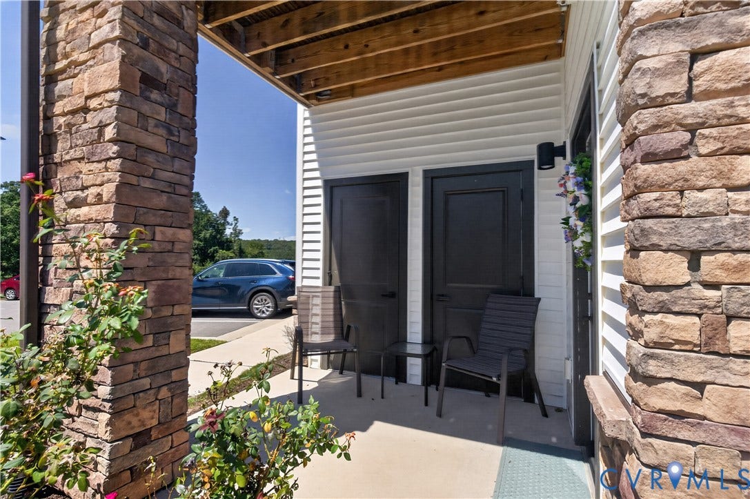 3900 Maze Runner Drive, #102, Chesterfield, VA 23112 Covered concrete porch featuring stacked stone columns, horizontal siding, and two dark-finish entry doors with wall-mounted lighting