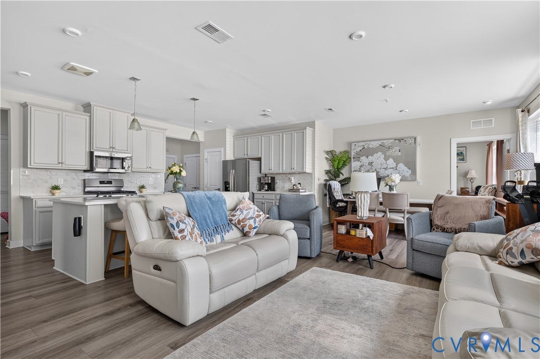 3900 Maze Runner Drive, #102, Chesterfield, VA 23112 Kitchen featuring light-toned cabinetry, stainless steel appliances, a peninsula with bar seating, and stone-finish backsplash, accented by wood-finish flooring