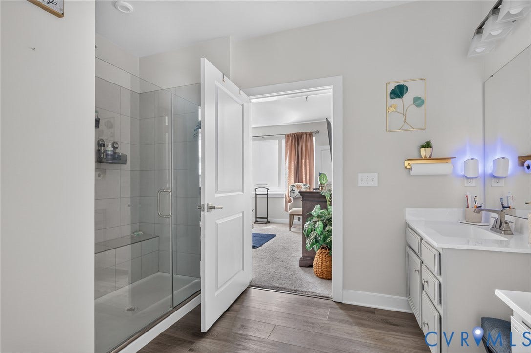 3900 Maze Runner Drive, #102, Chesterfield, VA 23112 Bathroom featuring a glass-enclosed walk-in shower with tiled surround and integrated bench, wood-finish flooring, vanity with solid-surface countertop, and multi-bulb vanity lighting