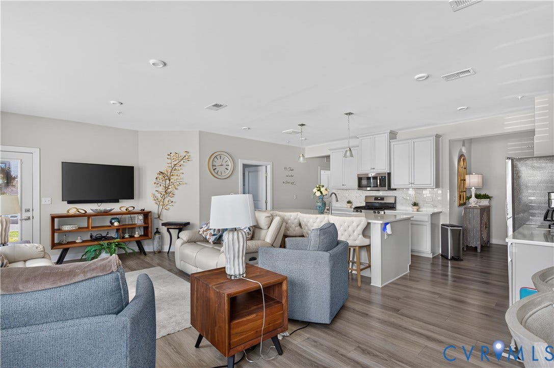 3900 Maze Runner Drive, #102, Chesterfield, VA 23112 Open-concept floor plan featuring wood-finish flooring, white shaker-style cabinetry, a central kitchen island with bar seating, and recessed ceiling lighting