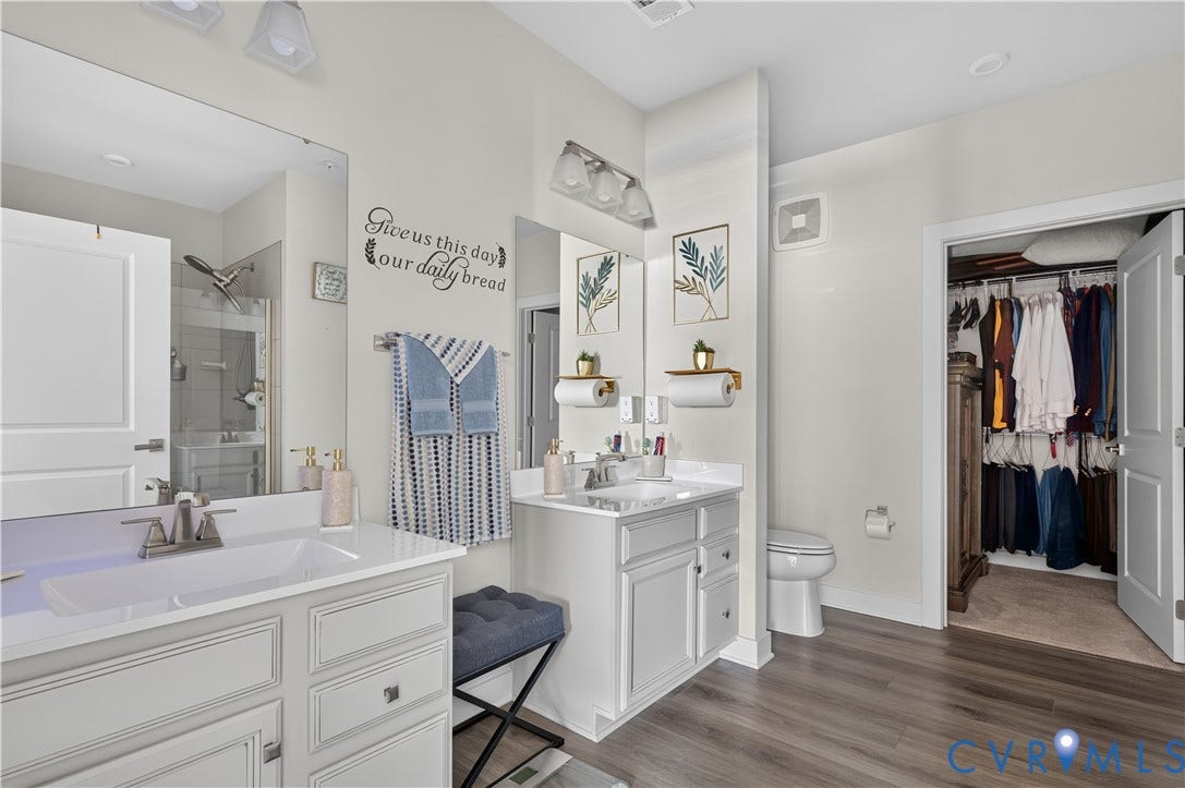 3900 Maze Runner Drive, #102, Chesterfield, VA 23112 Dual-sink vanity with white cabinetry and solid-surface countertops, full-width vanity mirrors, wood-finish flooring, and walk-in closet with built-in shelving