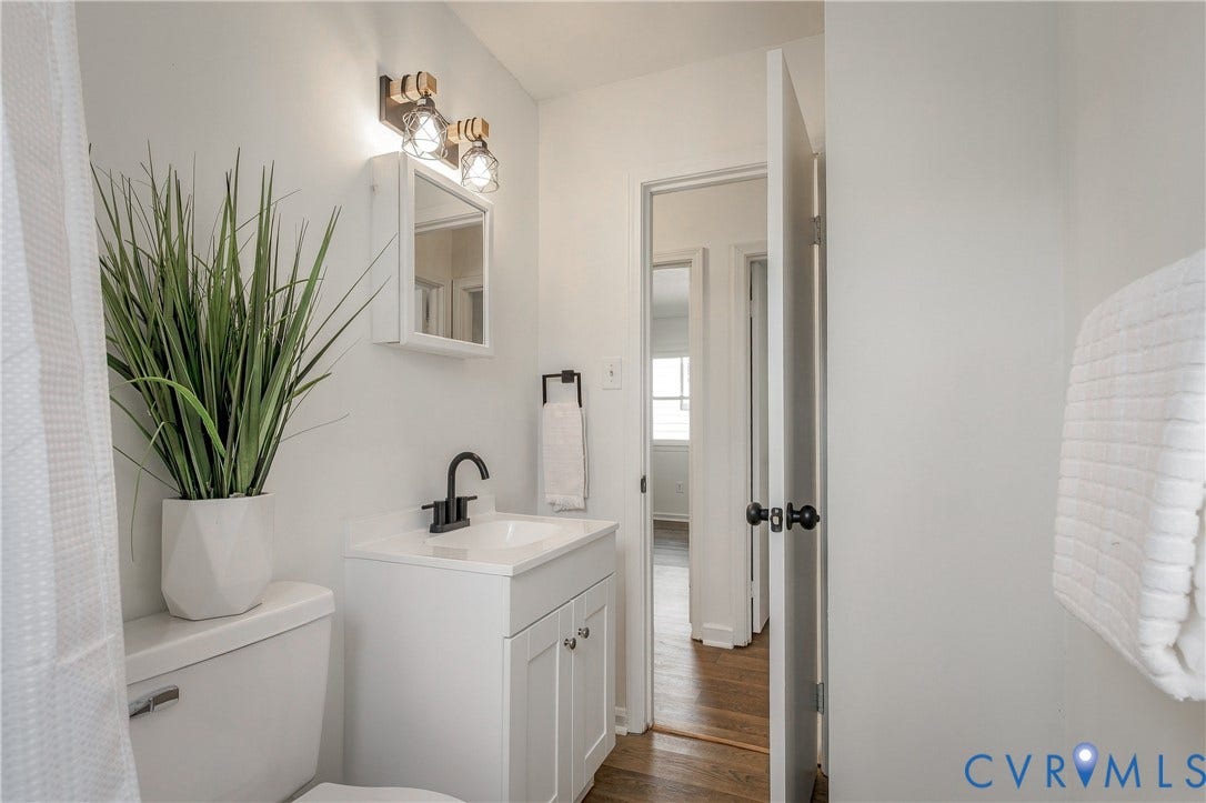 5429 Blueridge Avenue, Fulton, Richmond, VA 23231 White vanity with a rectangular sink, matte black faucet, wall-mounted medicine cabinet, dual-bulb industrial-style light fixture, and wood-finish flooring