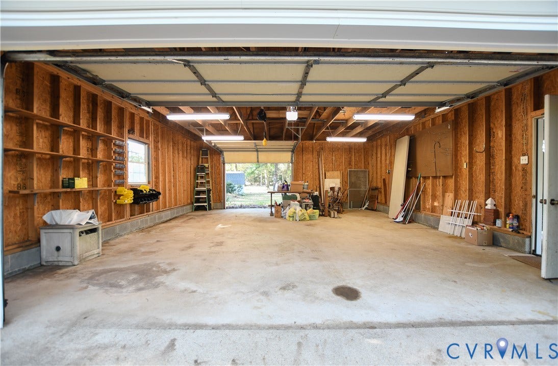 3486 Venter Road, Minors Pines, Aylett, VA 23009 Attached garage featuring exposed wood stud construction, concrete flooring, built-in wall shelving, and linear overhead lighting