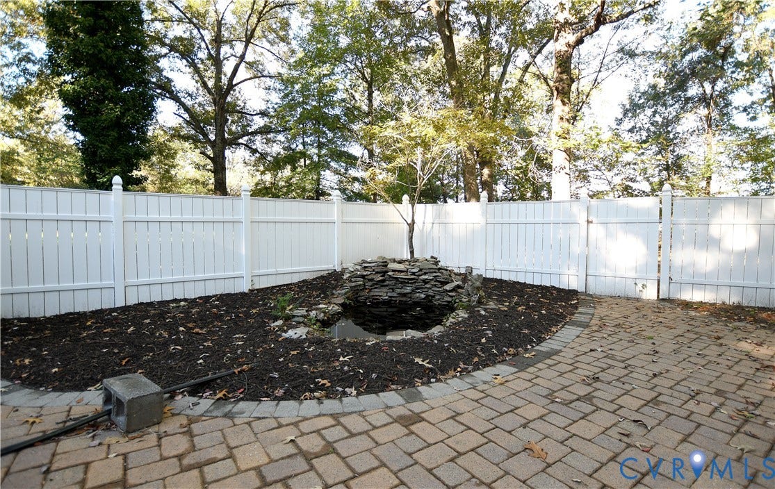3486 Venter Road, Minors Pines, Aylett, VA 23009 Backyard featuring a white vinyl privacy fence, stone water feature, paved patio area with a circular border, and mature trees