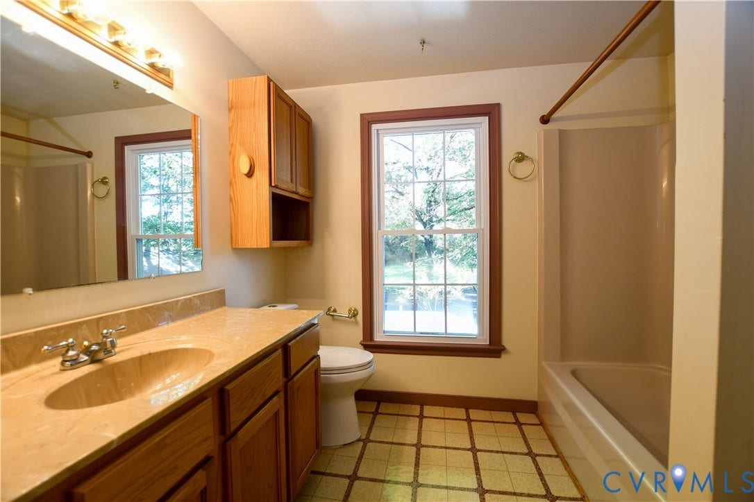 3486 Venter Road, Minors Pines, Aylett, VA 23009 Bathroom featuring a vanity with a solid-surface countertop, integrated sink, wooden cabinetry, wall-mounted mirror with integrated lighting, and a window with a paneled trim