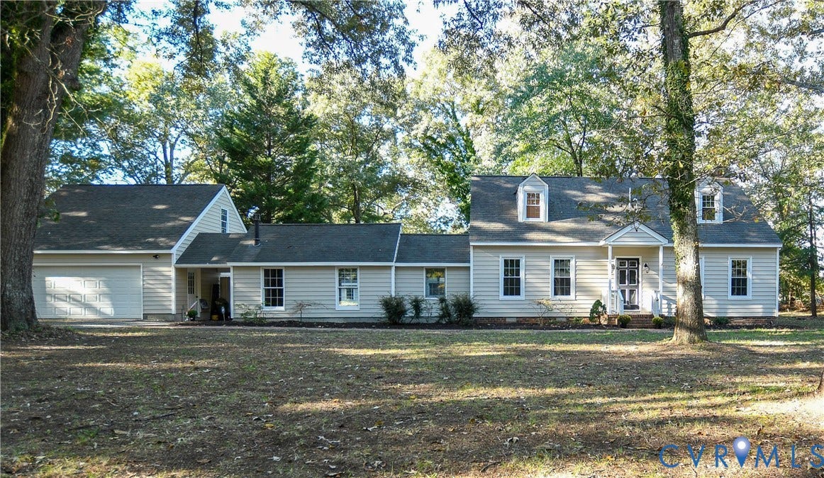 3486 Venter Road, Minors Pines, Aylett, VA 23009 Exterior featuring light-colored horizontal siding, dual front-facing dormer windows, an attached two-car garage, and mature trees across the property grounds