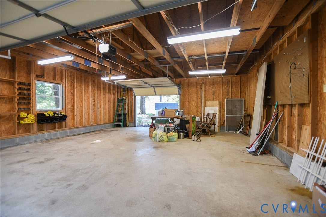 3486 Venter Road, Minors Pines, Aylett, VA 23009 Multi-car garage featuring exposed wood-stud walls, concrete flooring, linear fluorescent lighting, and built-in wall storage shelving