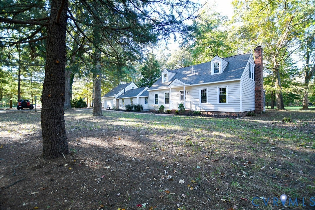 3486 Venter Road, Minors Pines, Aylett, VA 23009 Cape Cod style residence featuring light-colored horizontal siding, dual dormer windows, an exterior brick chimney, and an attached multi-car garage on a wooded lot