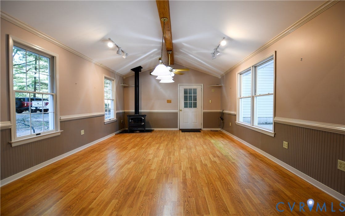 3486 Venter Road, Minors Pines, Aylett, VA 23009 Interior space featuring wood-finish flooring, vaulted ceilings with an exposed wooden beam, beadboard wainscoting, a free-standing metal wood-burning stove, and multiple large windows