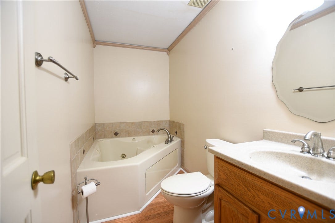 3486 Venter Road, Minors Pines, Aylett, VA 23009 Corner soaking tub with tile surround, wood-finish cabinetry, integrated vanity countertop with sink, and wall-mounted vanity mirror