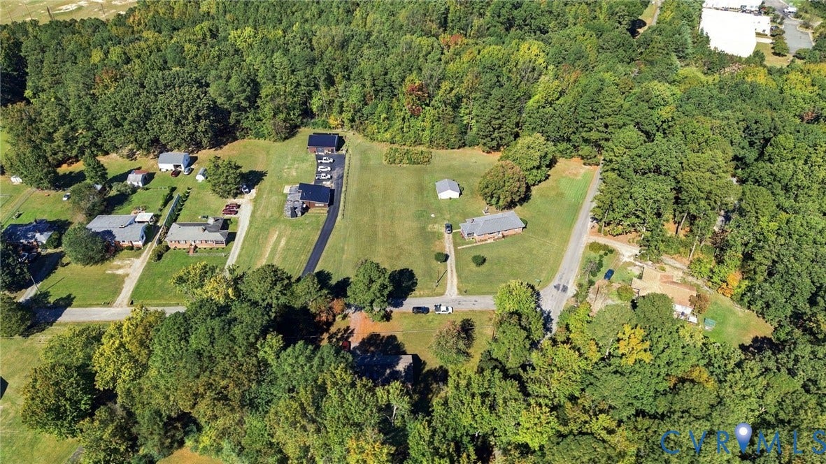 Aerial perspective featuring expansive acreage, mature perimeter trees, paved driveway, and open grass lawns