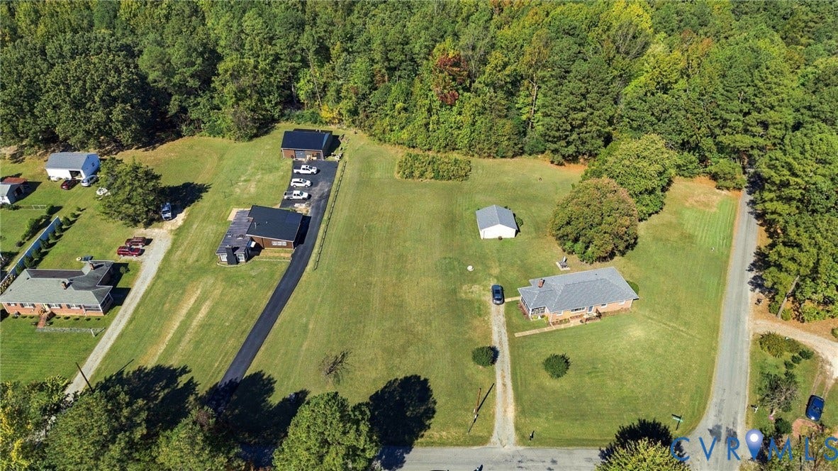 Aerial view featuring expansive acreage, mature tree canopy, asphalt driveway, and detached storage structure
